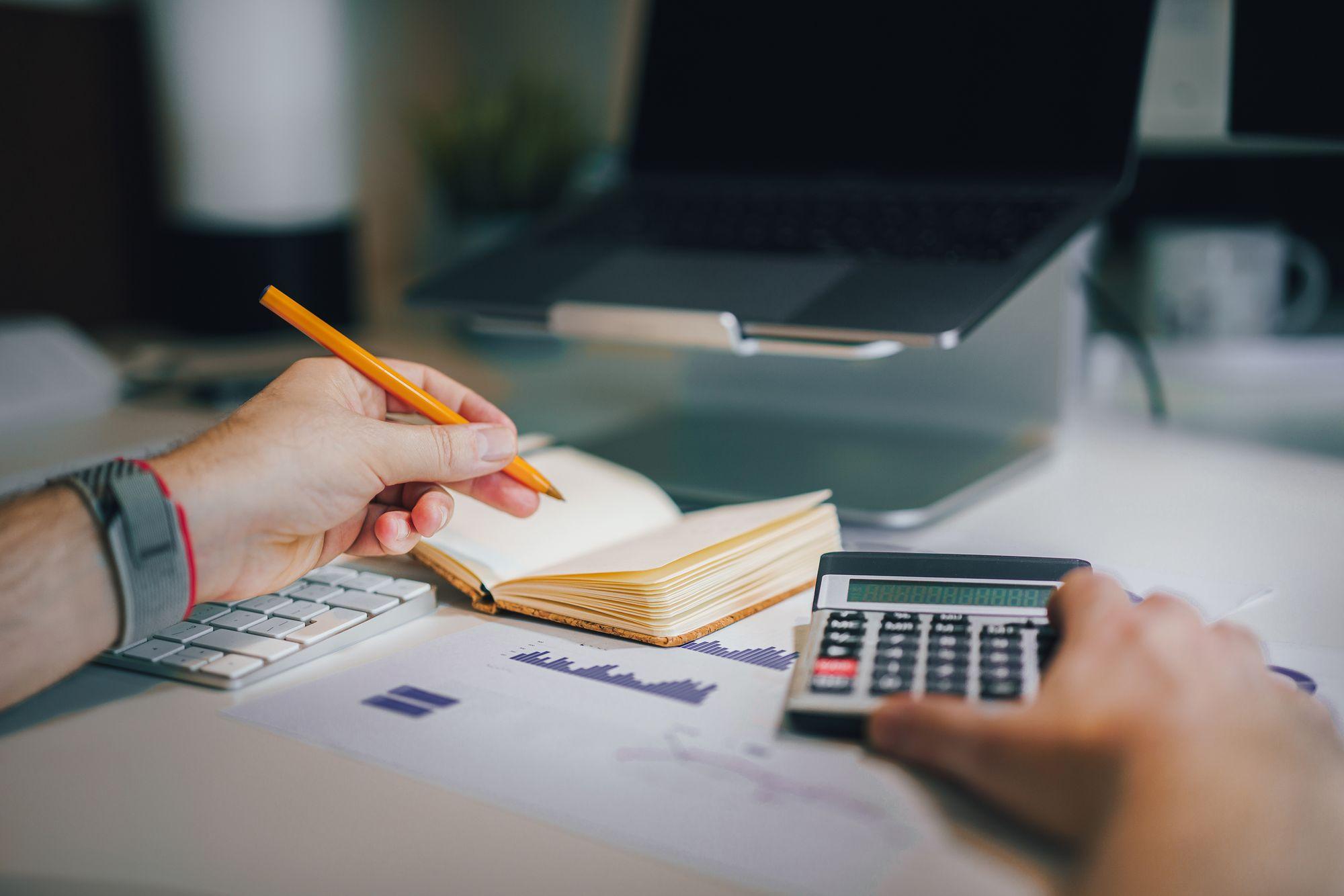 Accountant reviewing financial reports with a calculator and laptop, representing Edu Accounting & Auditors' accounting services