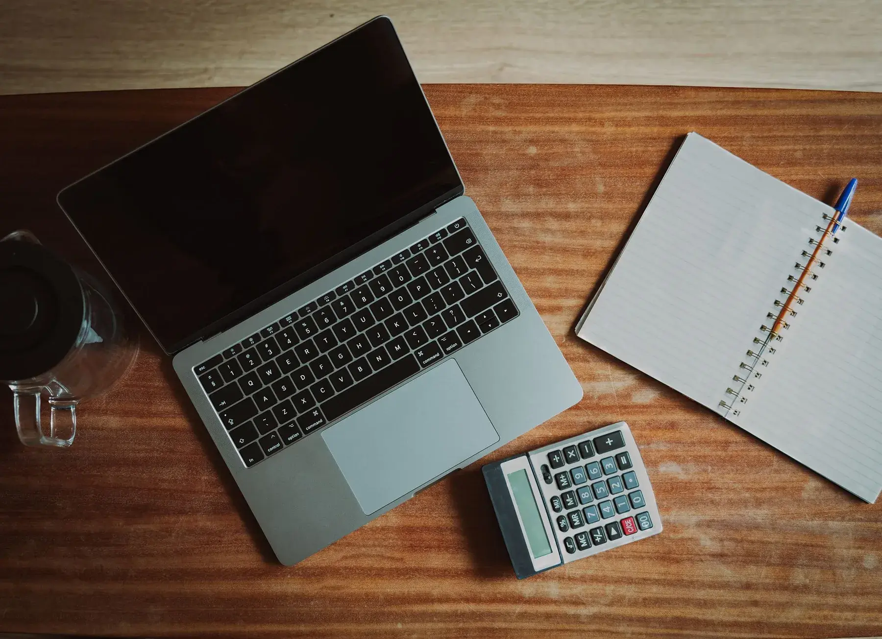 A laptop, calculator and notebook arranged on a wooden desk, representing Edu Accounting & Auditors' payroll services